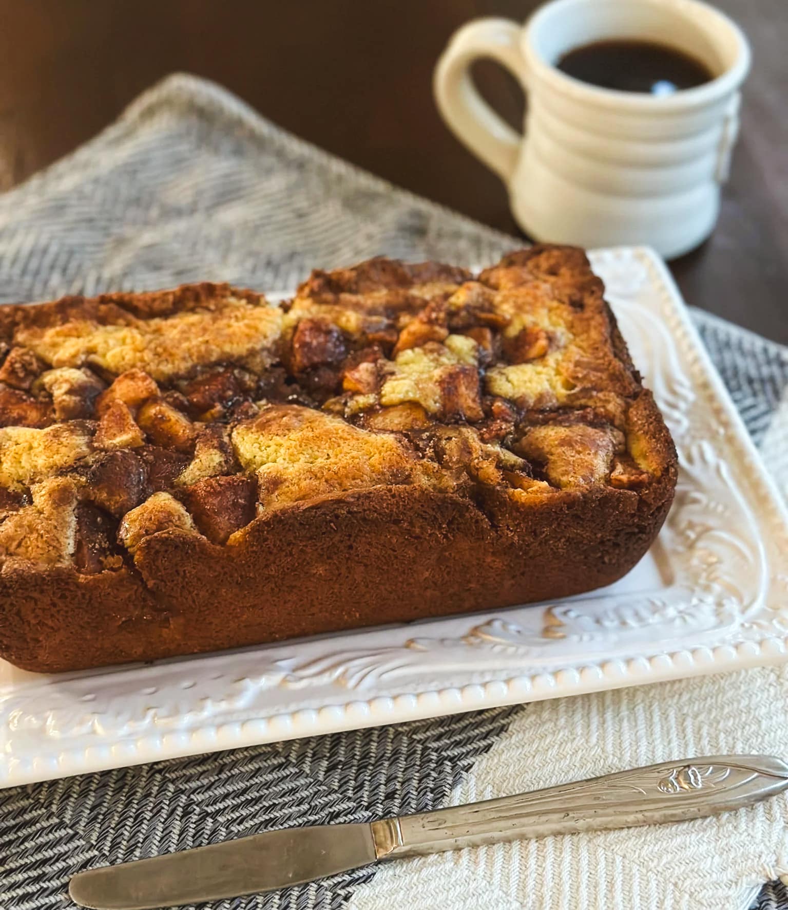 Homemade apple fritter bread topped with cinnamon-spiced apples beside a cup of coffee