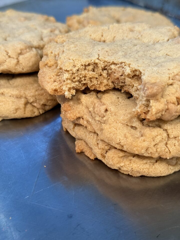 Pile of bakery-style peanut butter cookies with a cracked, tender texture and buttery shine